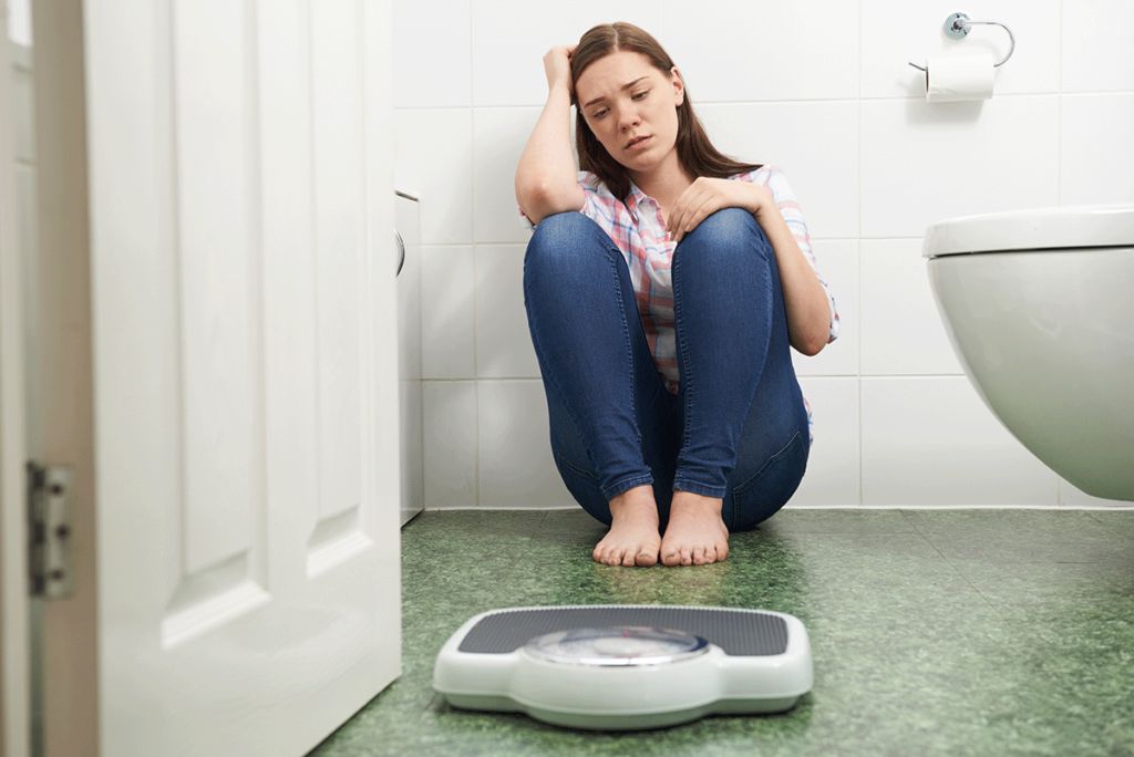 woman looks at scale in bathroom and considers the main causes of bulimia